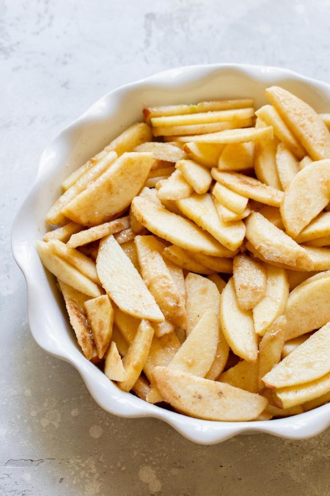 Sliced apples coated in cinnamon and sugar in a round baking dish.