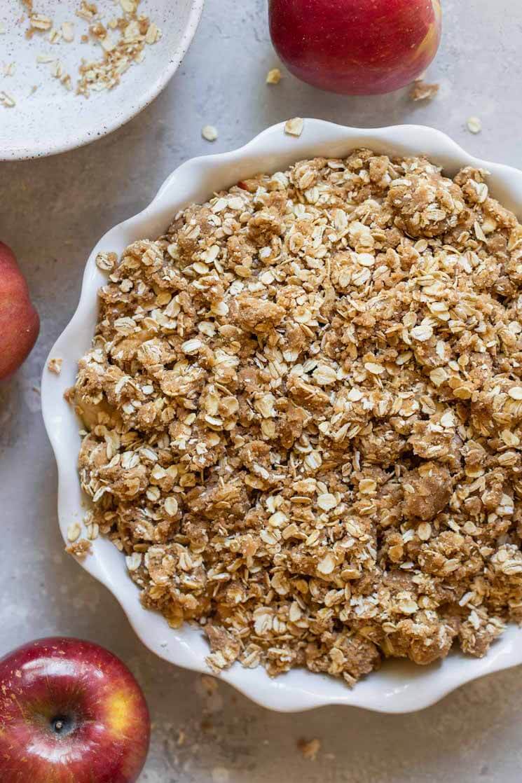 An apple crisp ready to go in the oven surrounded by more apples.