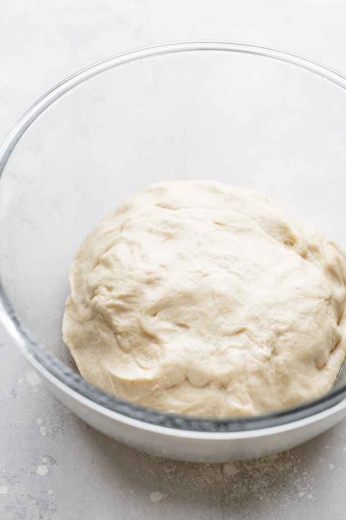 A glass mixing bowl holding the finished dough that needs to rise.