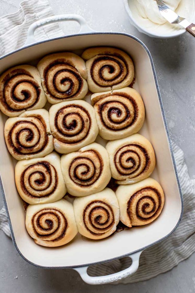 A white baking pan holding cinnamon rolls that are cooling before being topped with icing.