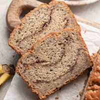 Two slices of cinnamon banana bread laying on a cutting board next to the rest of the loaf.