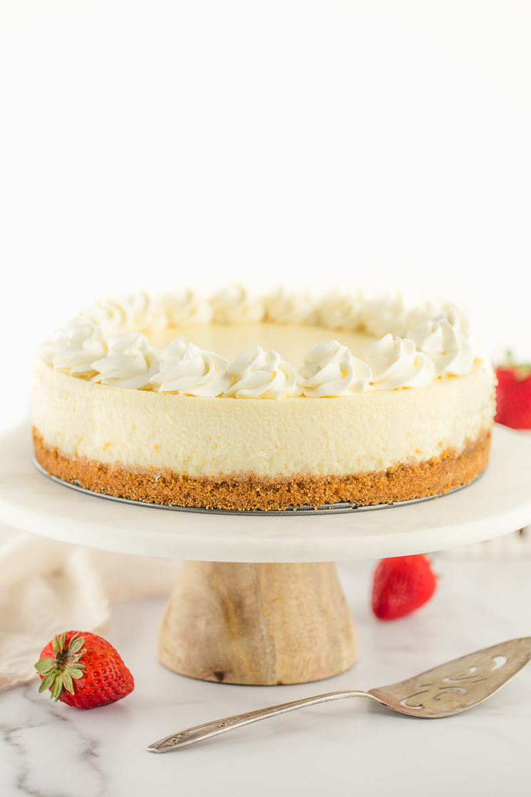 A cheesecake topped with whipped cream on top of a marble cake stand.