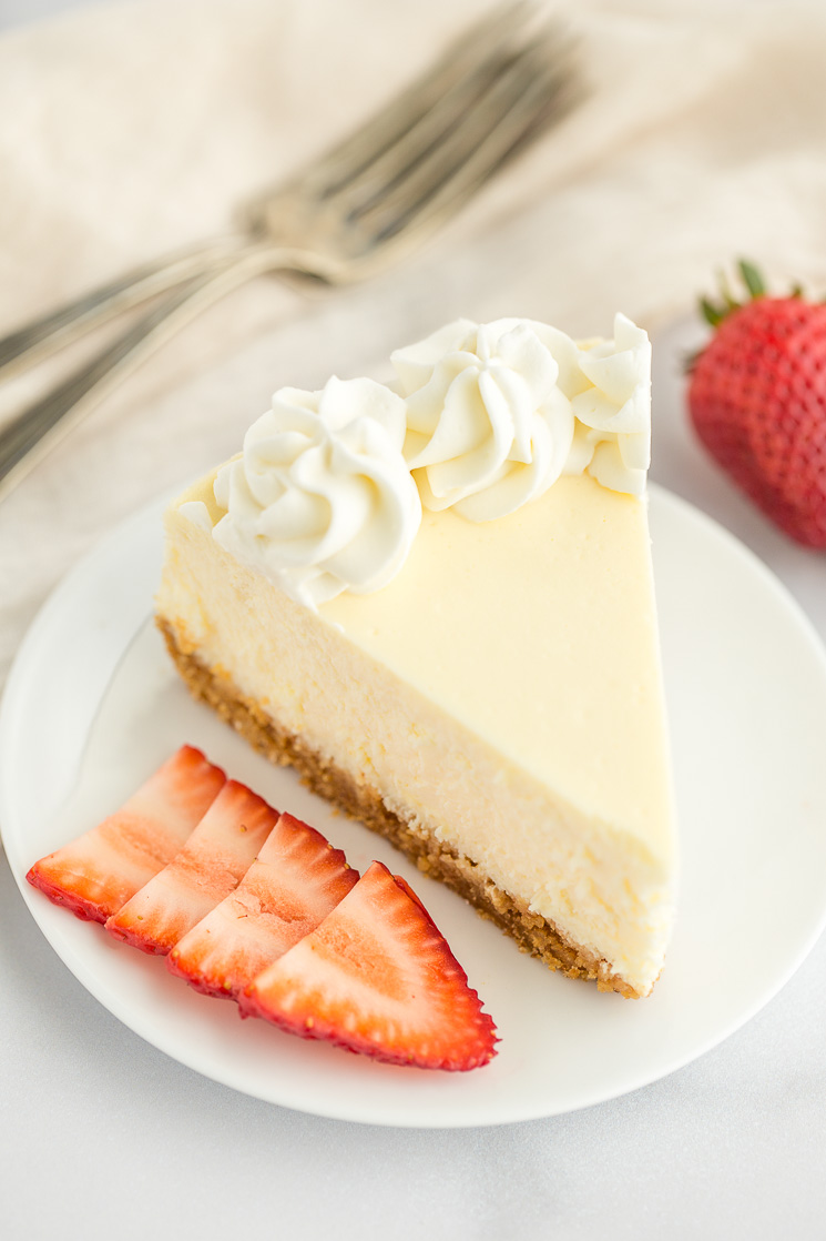 A slice of cheesecake topped with whipped cream on a white plate.