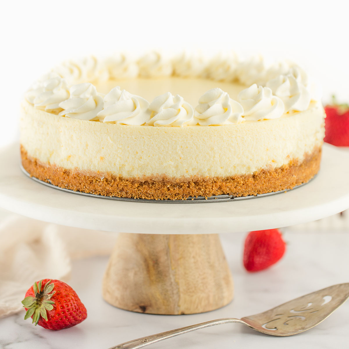 A cheesecake topped with whipped cream sitting on a marble cake stand.