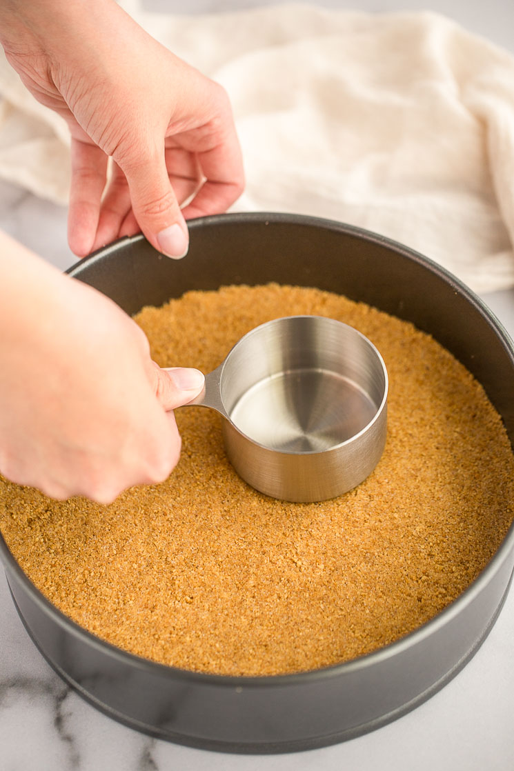 A springform pan filled with an unbaked graham cracker crust.