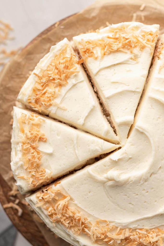 An overhead view of a frosted coconut layer cake on a cake stand. Three slices have been cut. 