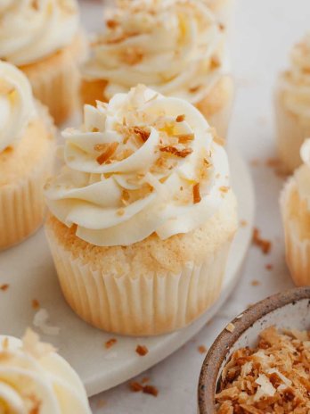 Several coconut cupcakes topped with toasted coconut.