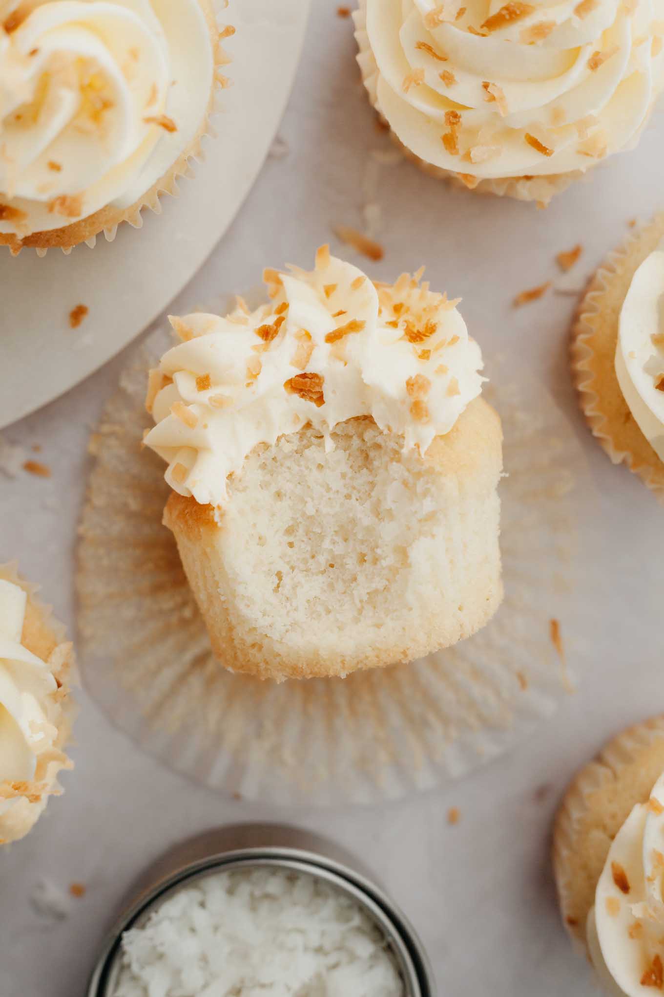 An overhead view of a coconut cupcake with a bite missing, laying on its side. 