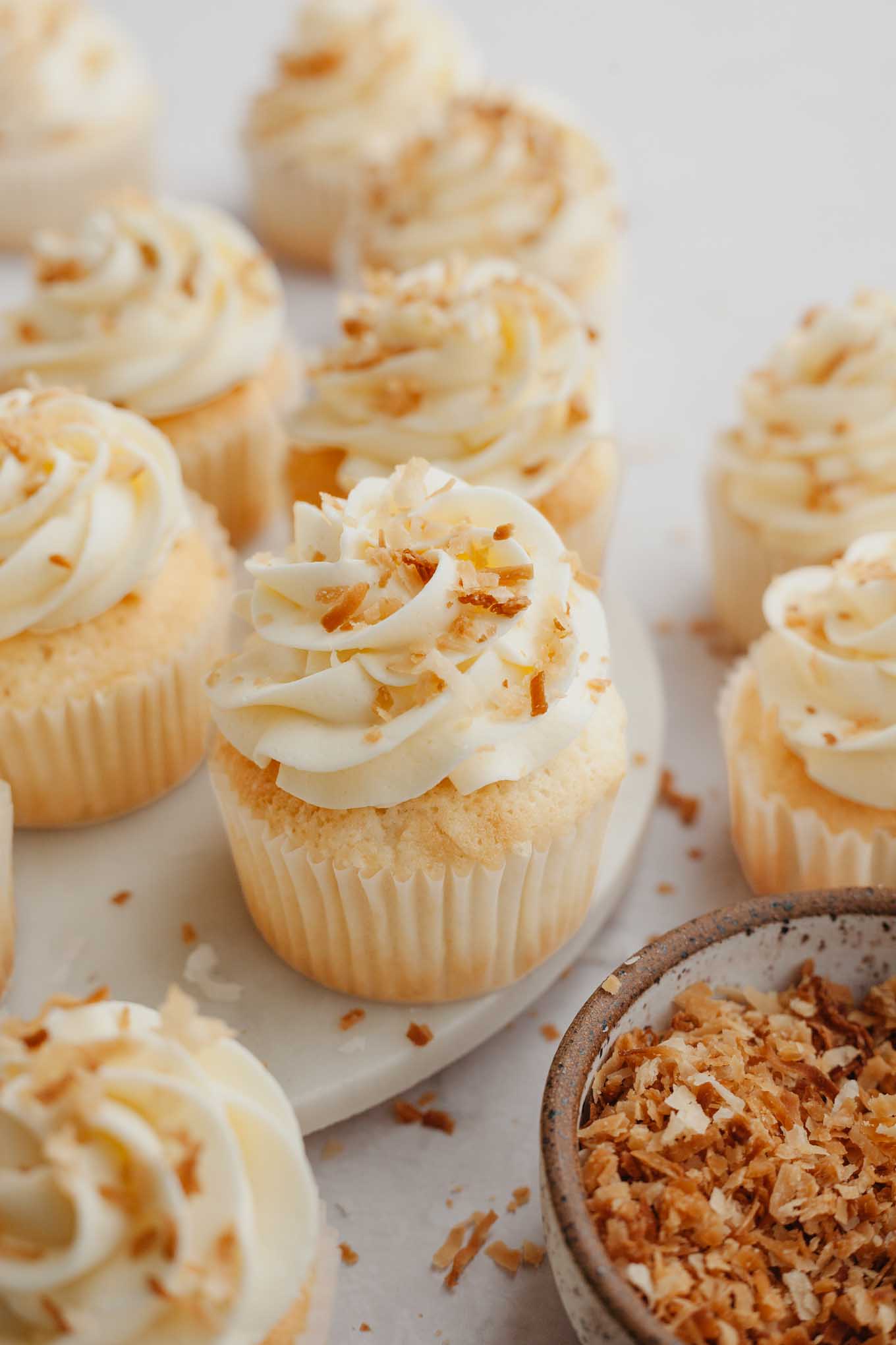 Several coconut cupcakes topped with coconut frosting and toasted coconut.