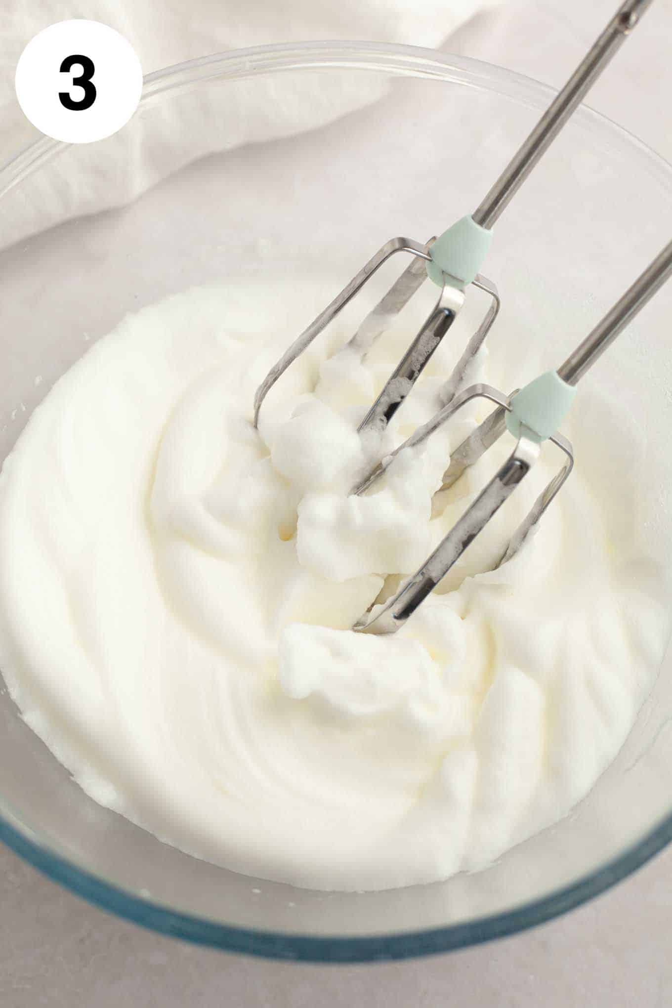 An overhead view of whipped egg whites in a glass mixing bowl. 