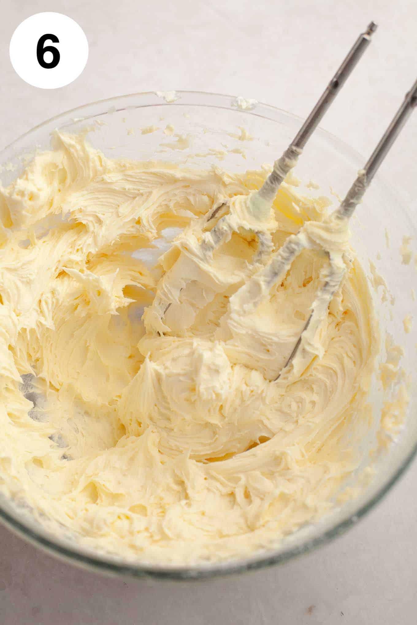 Creamy coconut frosting in a glass mixing bowl, with the beaters from an electric mixer. 