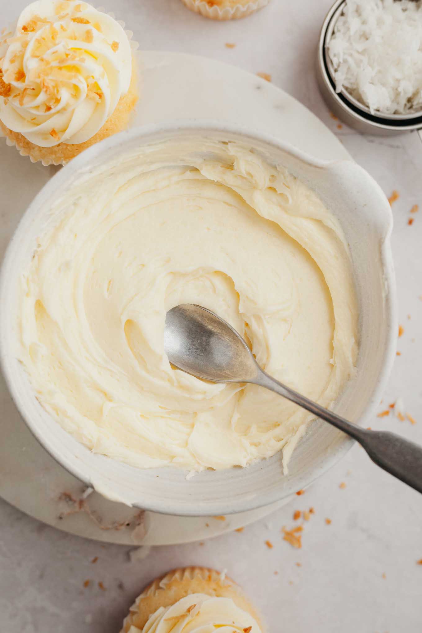 A bowl of coconut frosting with a spoon resting in it.