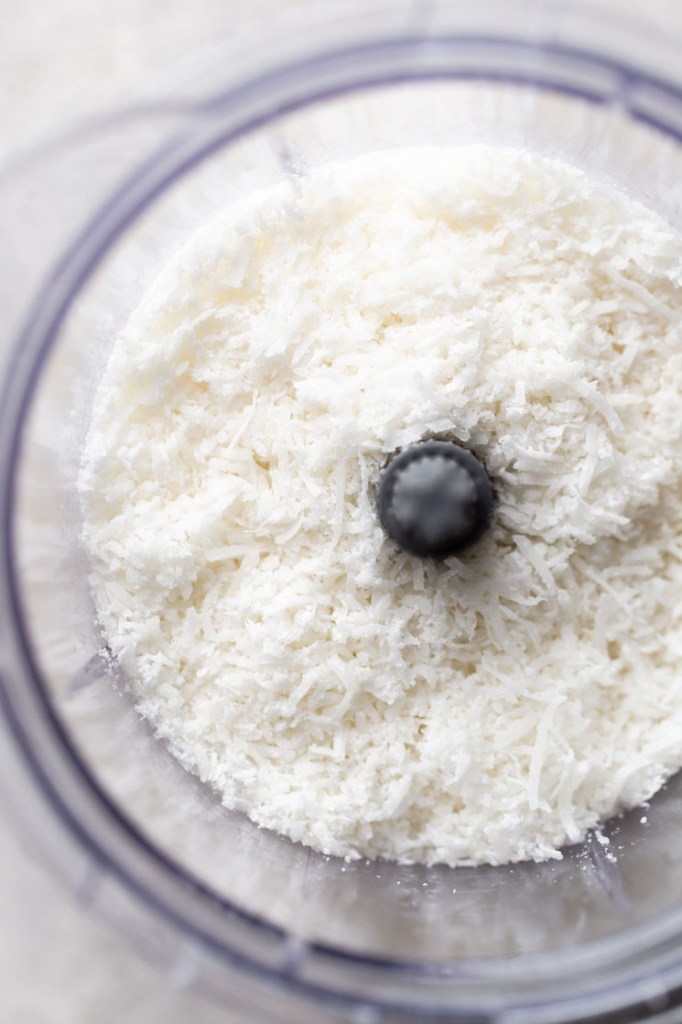 Overhead view of sweetened shredded coconut in a food processor. 