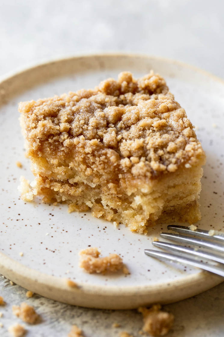 A single piece of coffee cake resting on a rustic plate with a bite taken out of the corner.