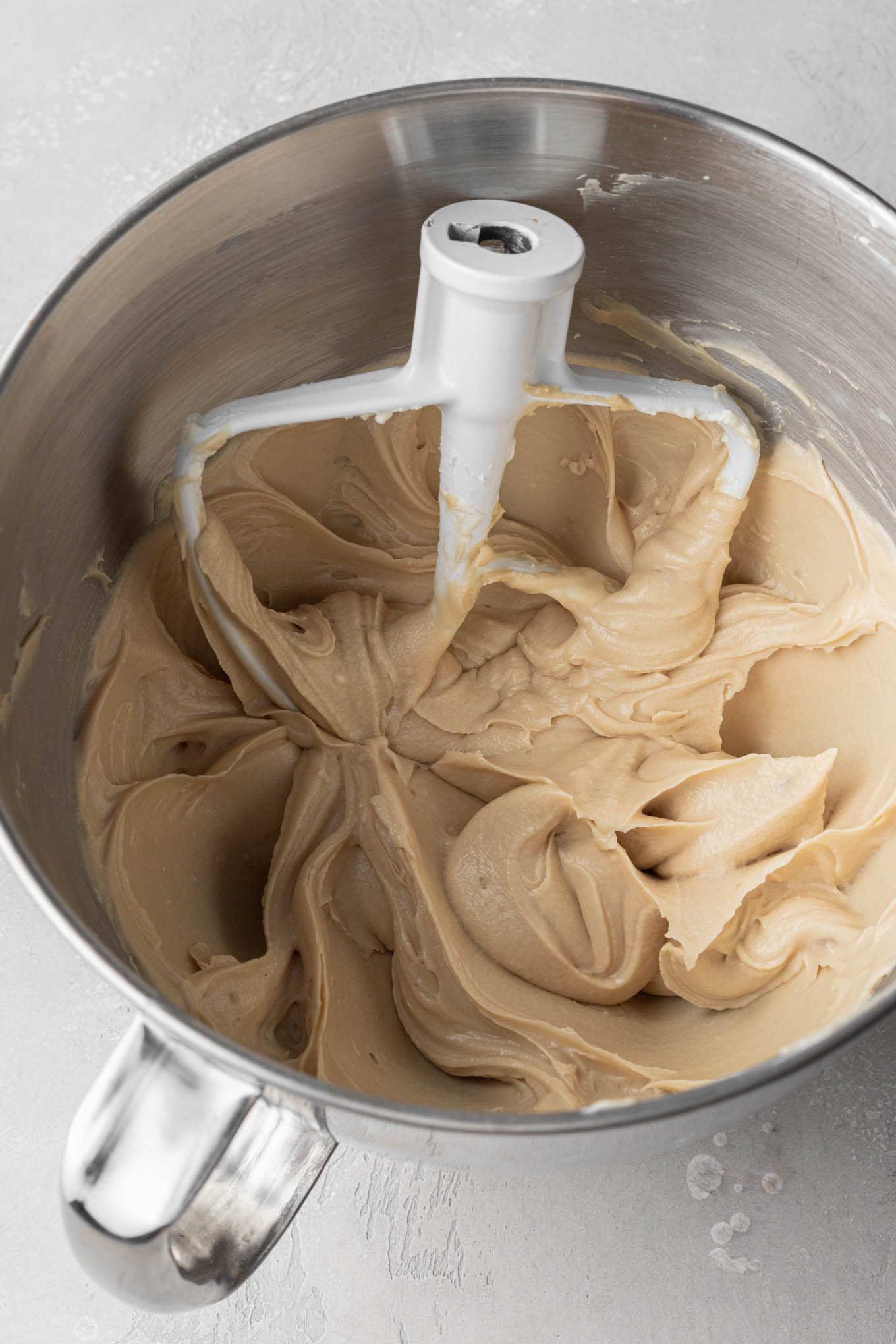 An overhead view of edible cookie dough dip mixture in a mixing bowl. A paddle attachment rests in the bowl. 