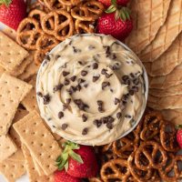 An overhead view of cookie dough dip in a bowl. The bowl is surrounded by pretzels, graham crackers, strawberries, and pieces of waffle cones.