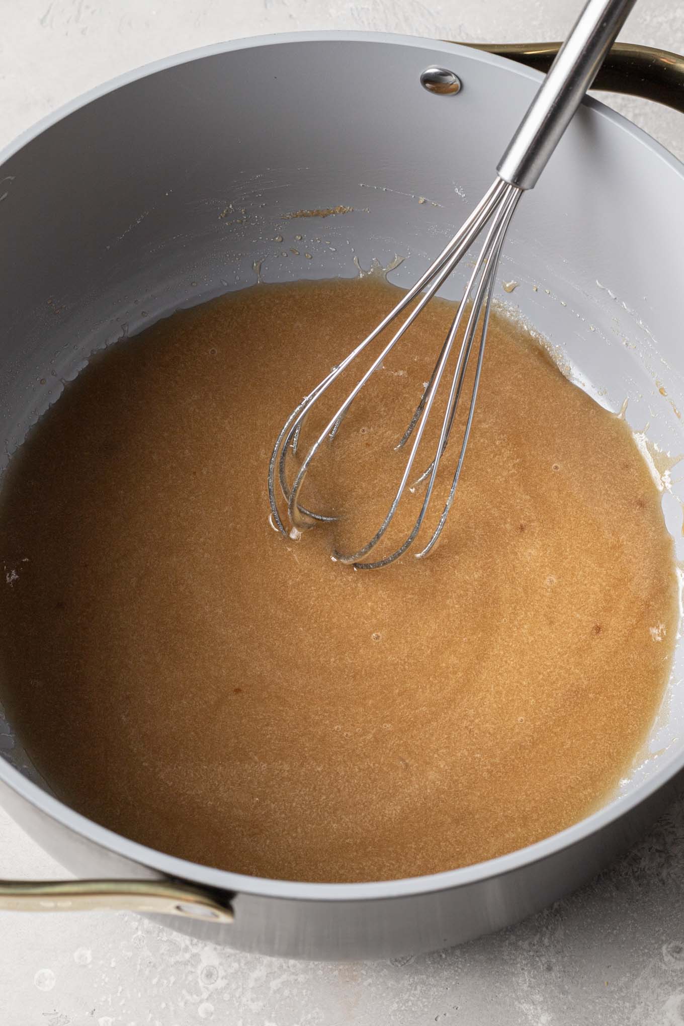 An overhead view of corn syrup and sugar in a saucepan, with a whisk. 