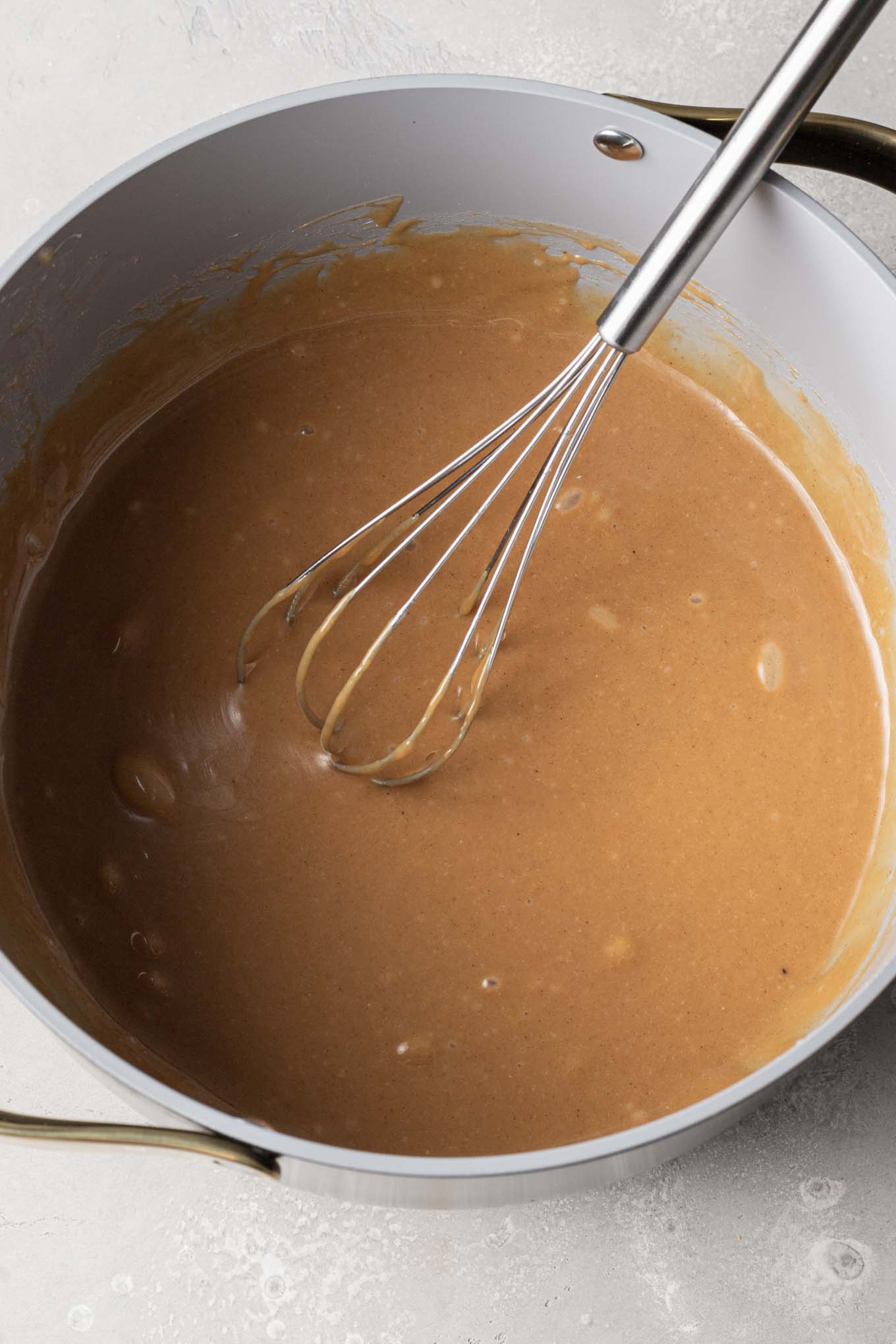 An overhead view of the melted peanut butter mixture in a saucepan, with a whisk. 