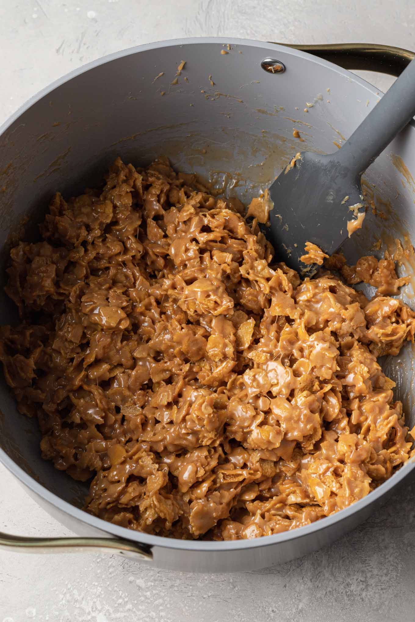 An overhead view of the cornflake cookie mixture in a saucepan, with a rubber spatula. 