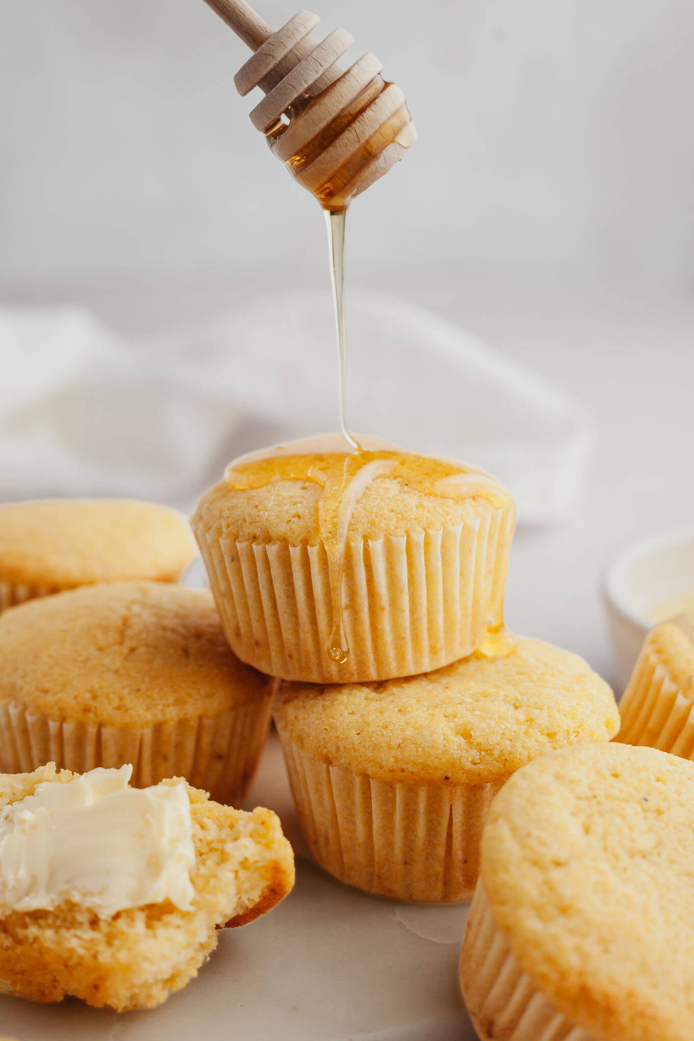 An action shot showing honey being drizzled over a stack of sweet cornbread muffins. 