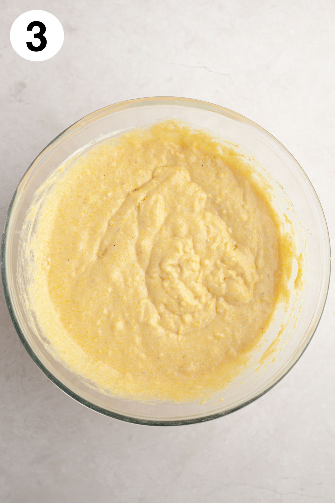 An overhead view of cornbread muffin batter in a glass mixing bowl.