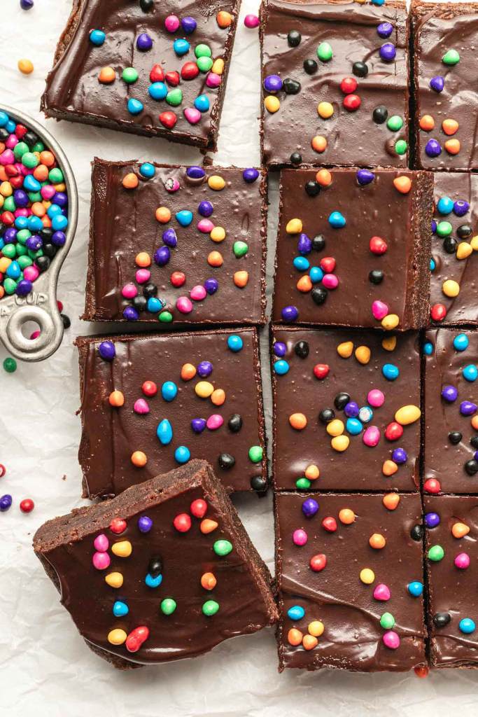 An overhead view of sliced cosmic brownies. A small metal measuring up with rainbow chips is beside the brownies.