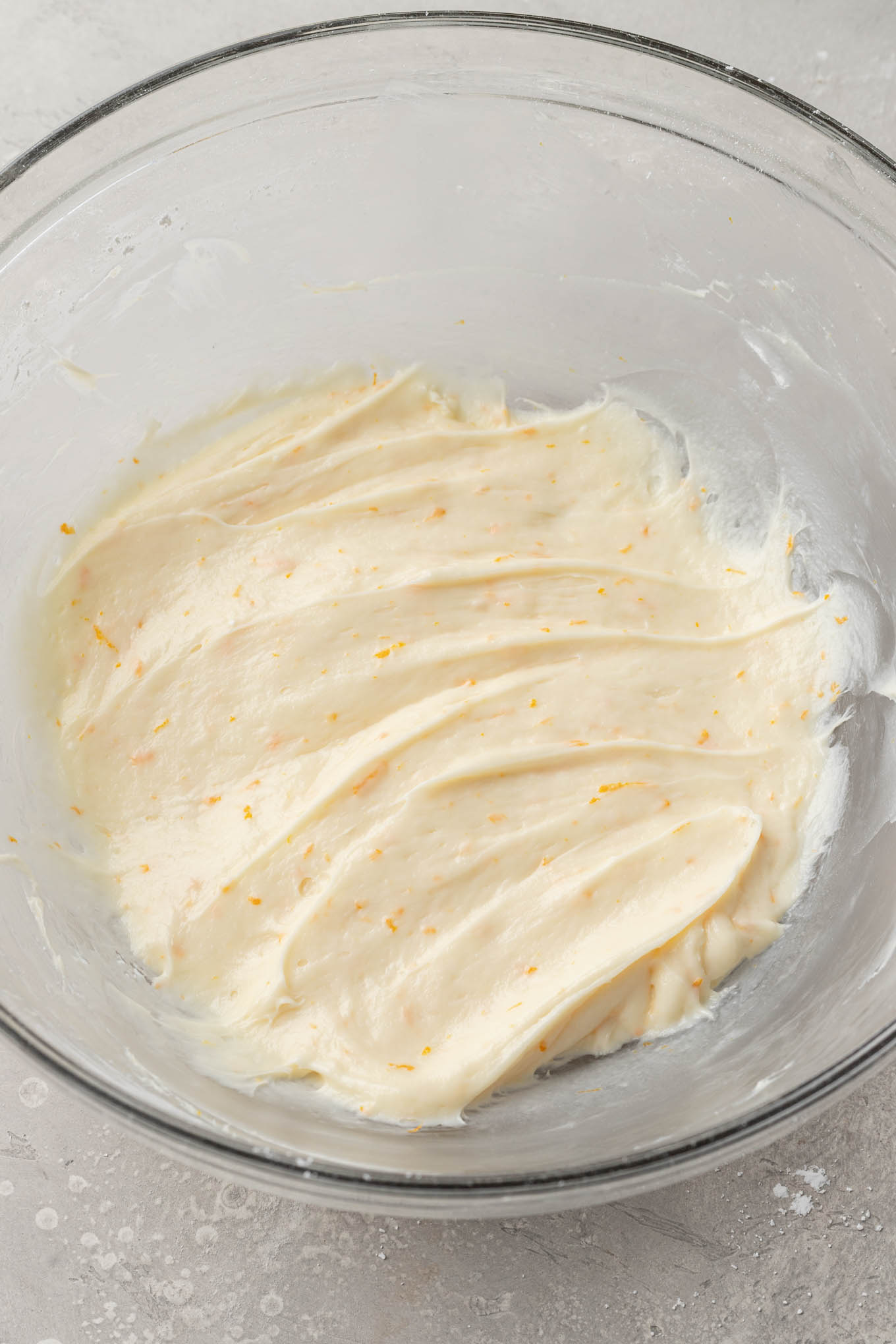 An overhead view of orange cream cheese frosting in a glass mixing bowl. 