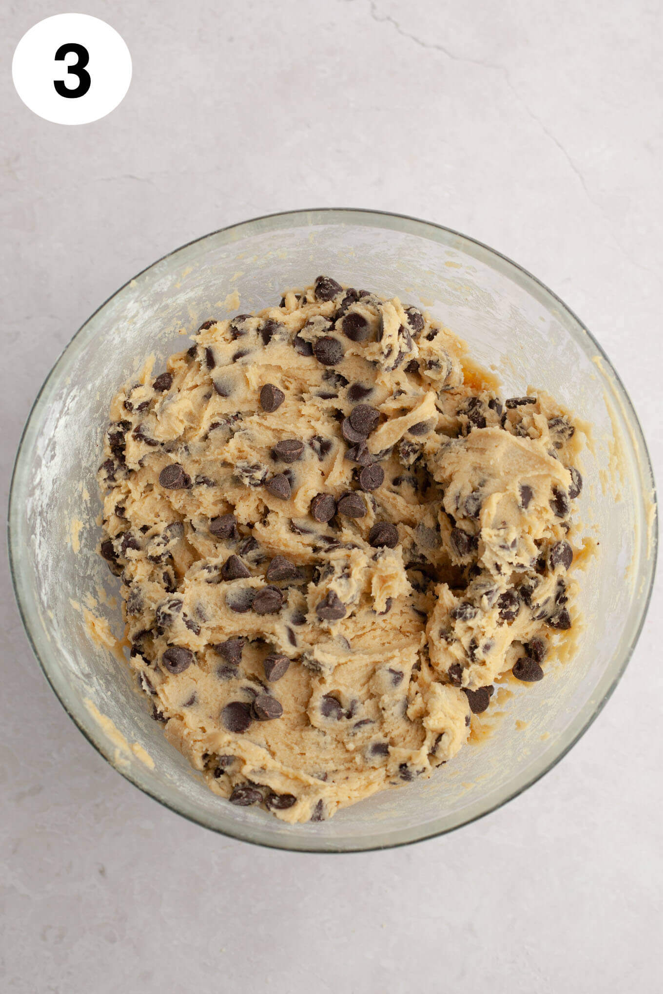 An overhead view of chocolate chip cream cheese cookie dough in a glass mixing bowl. 