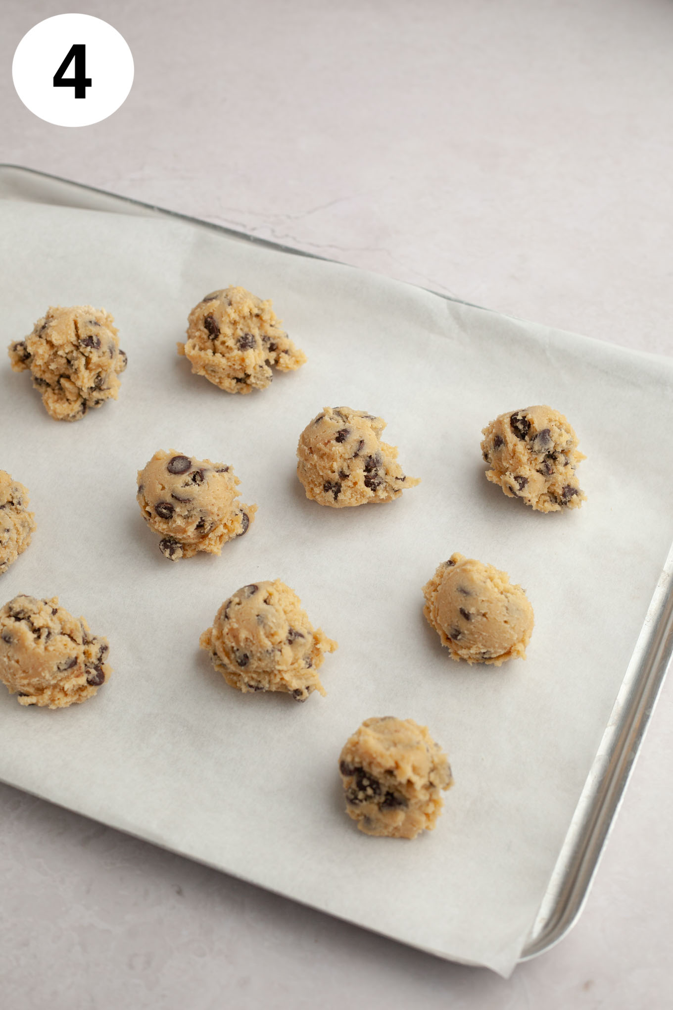 Scoops of cream cheese chocolate chip cookie dough on a parchment paper-lined baking sheet.