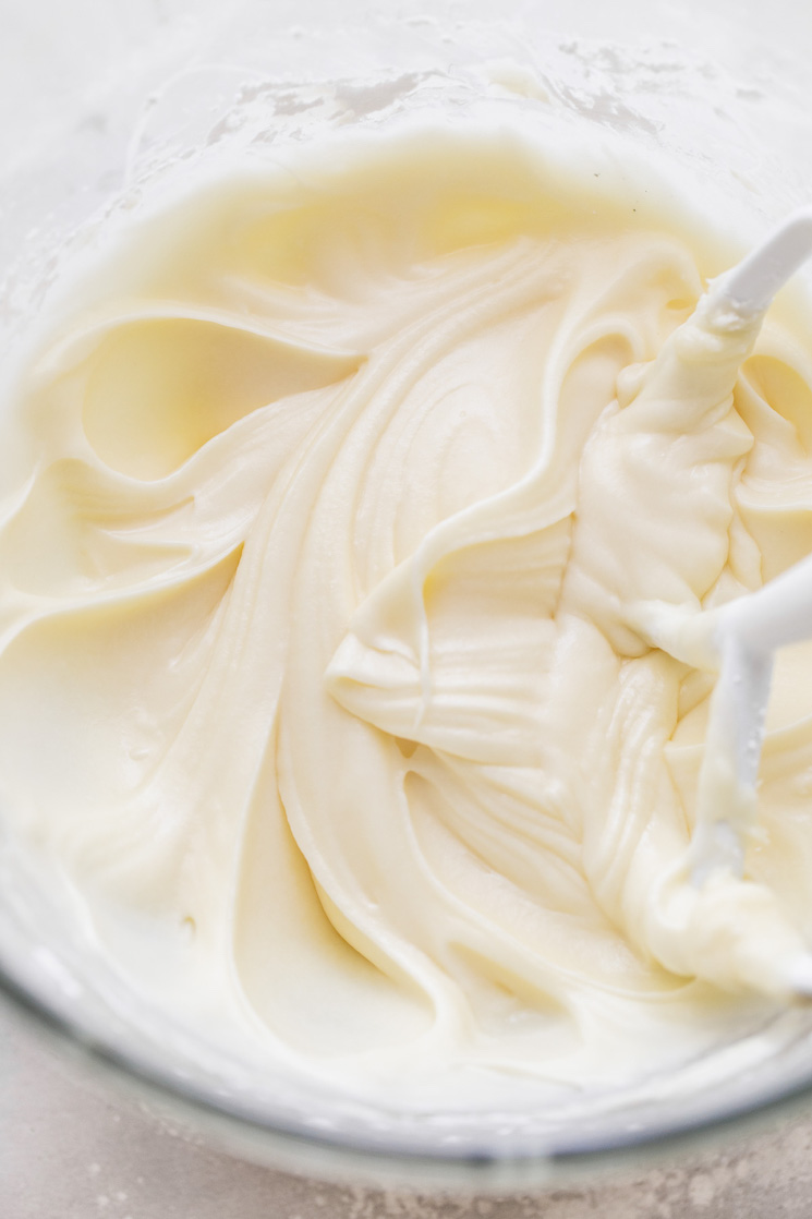 A glass mixing bowl with cream cheese frosting and the beater that was used to mix it up.