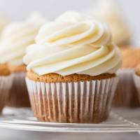 A cupcake topped with cream cheese frosting on a round cooling rack.