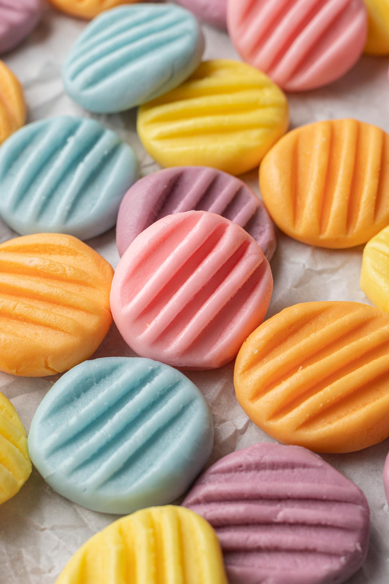 An up-close view of pastel-colored mints strewn over parchment paper. 