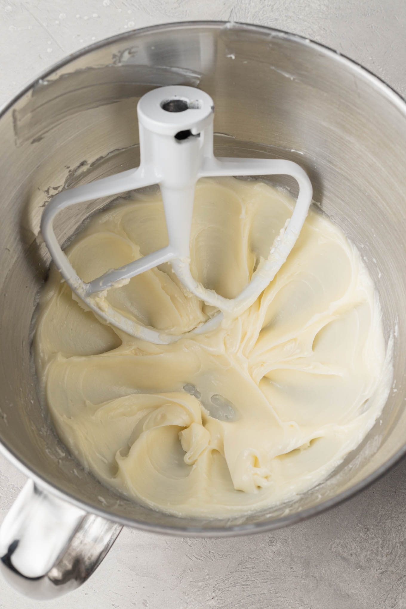 An overhead view of beaten cream cheese mint mixture in a mixing bowl, with a paddle attachment. 