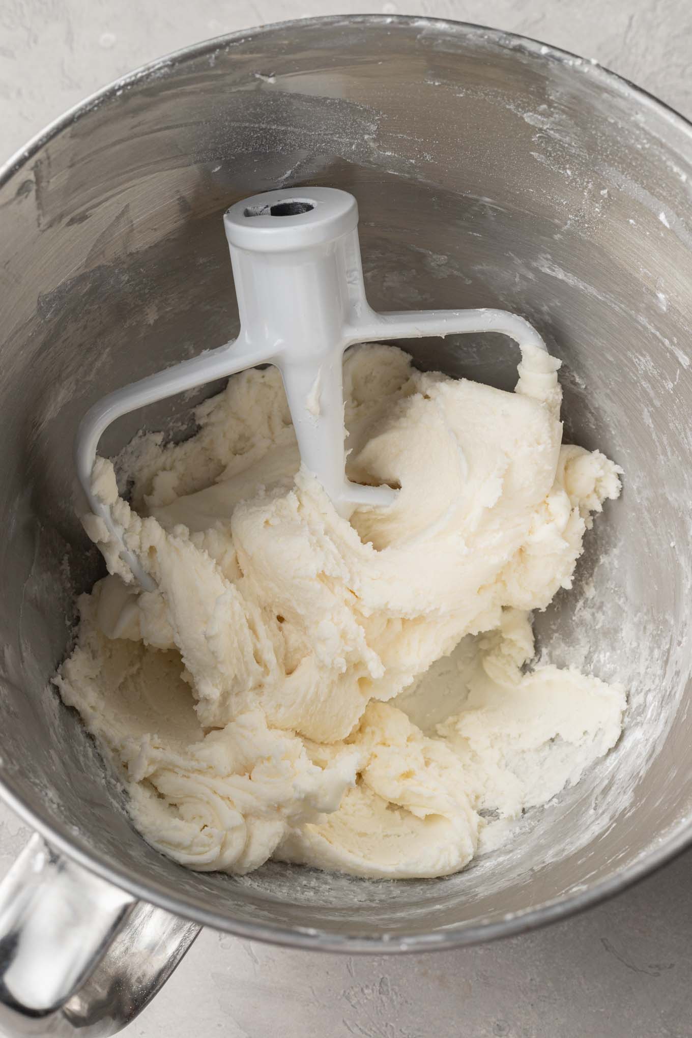 An overhead view of beaten cream cheese mint mixture in a mixing bowl, with a paddle attachment. 