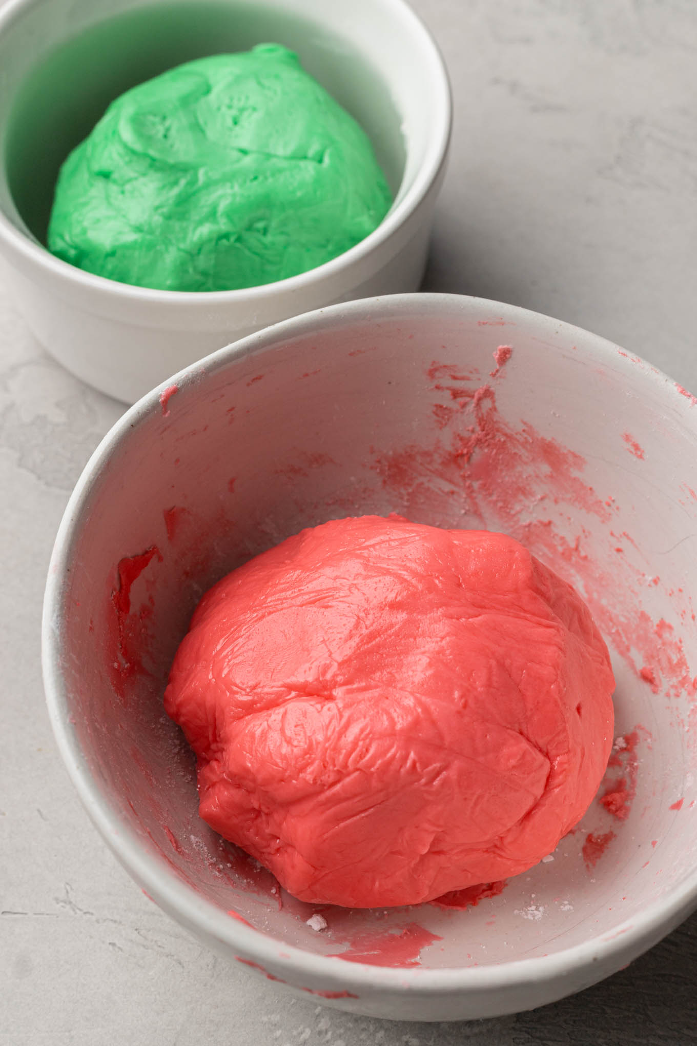 Red and green balls of homemade mint mixture in two separate mixing bowls. 