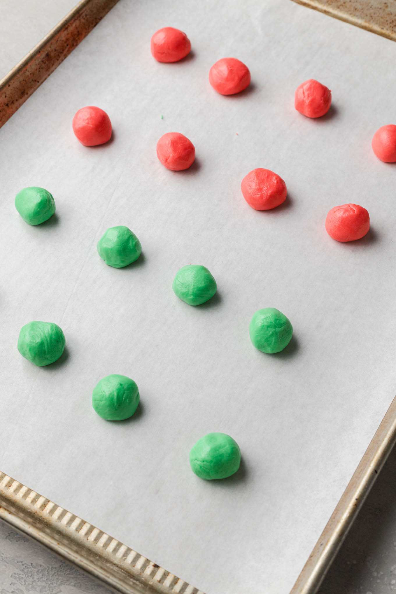 Red and green balls of Christmas cream cheese mint mixture on a parchment paper-lined baking sheet. 