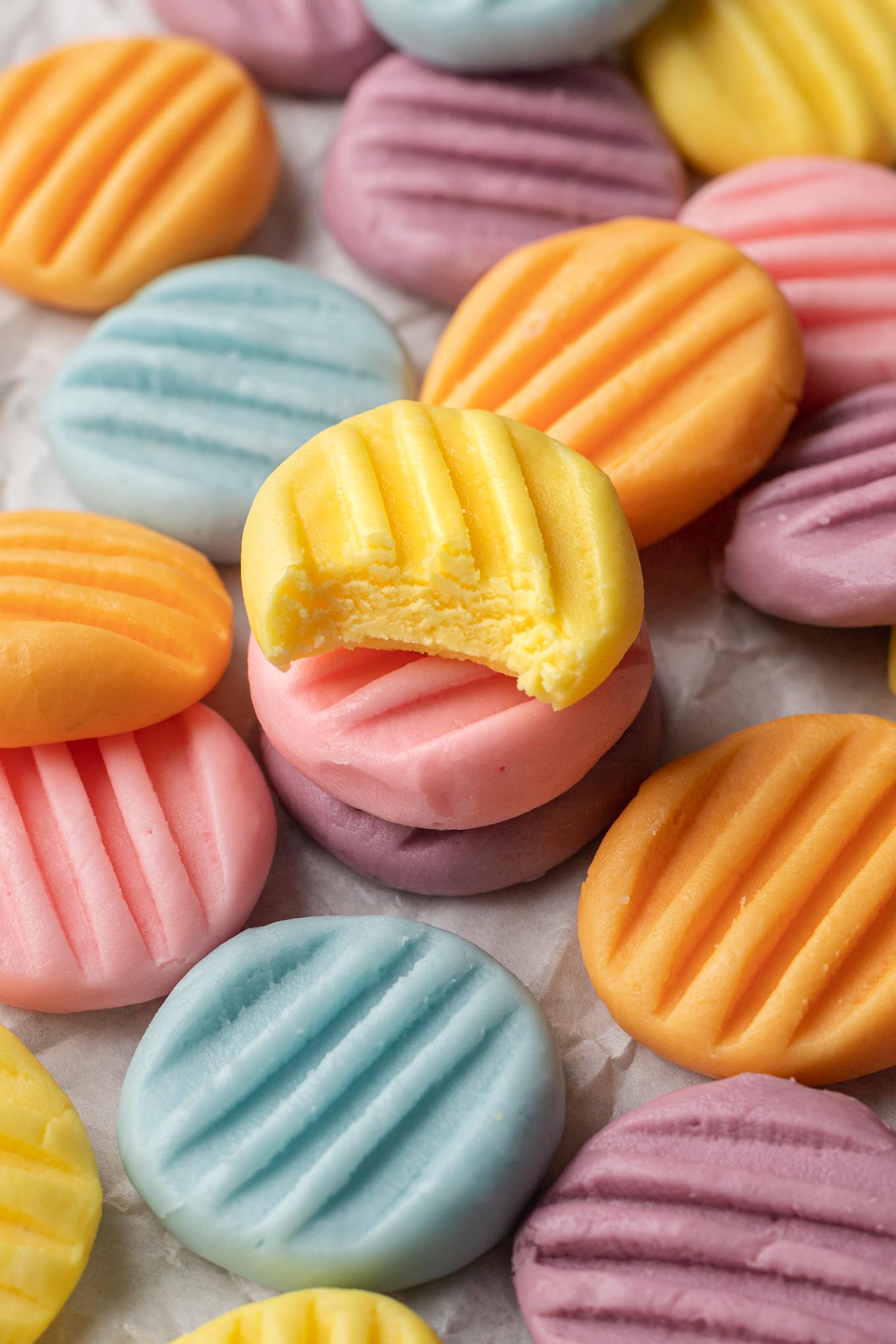 An up-close view of pastel-colored mints strewn over parchment paper. 