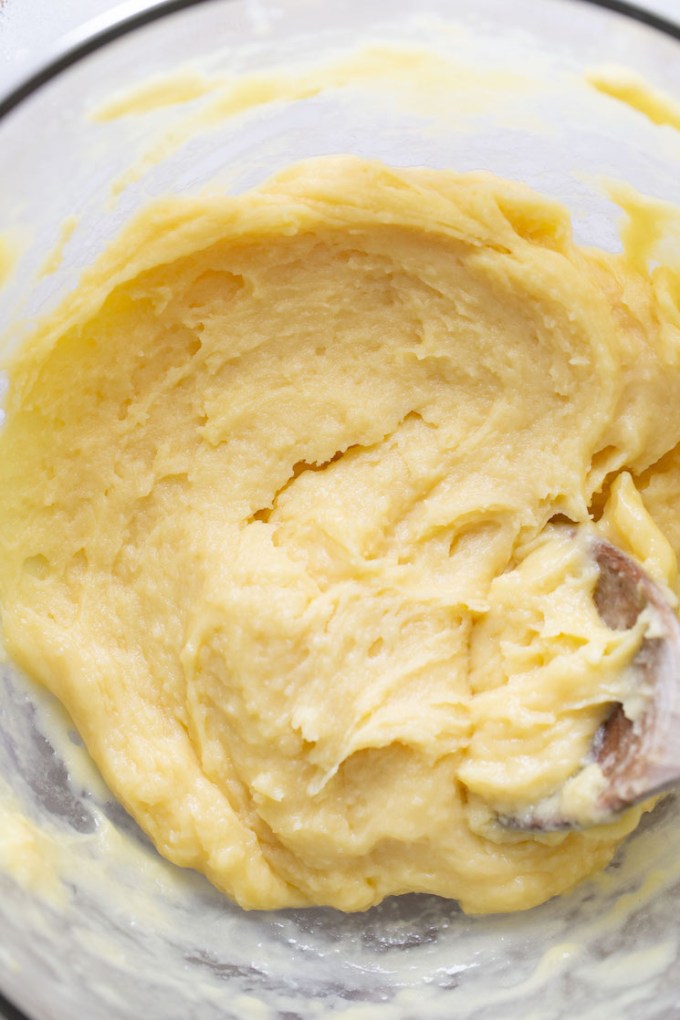 Choux pastry dough in a large glass bowl with a wooden spoon.