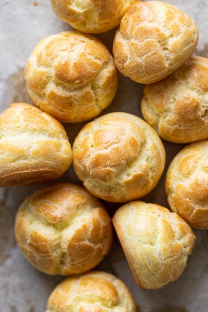 Baked cream puff shells piled on a countertop.