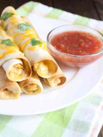 Five baked chicken taquitos on a white plate with a dish of salsa.