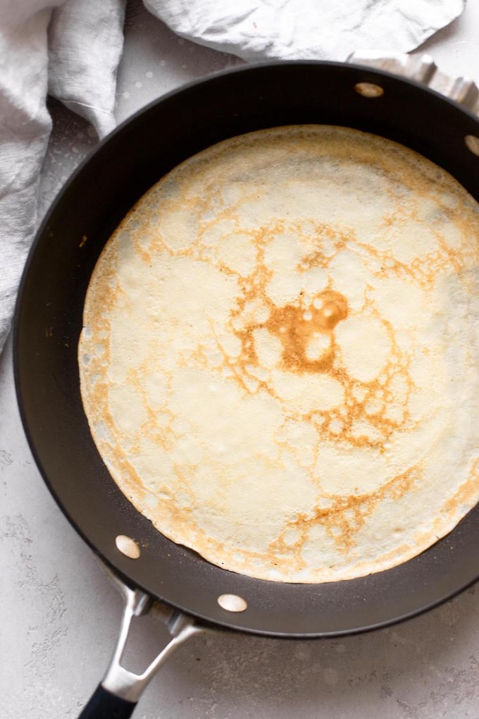 Overhead view of a cooked homemade crepe in a nonstick skillet.