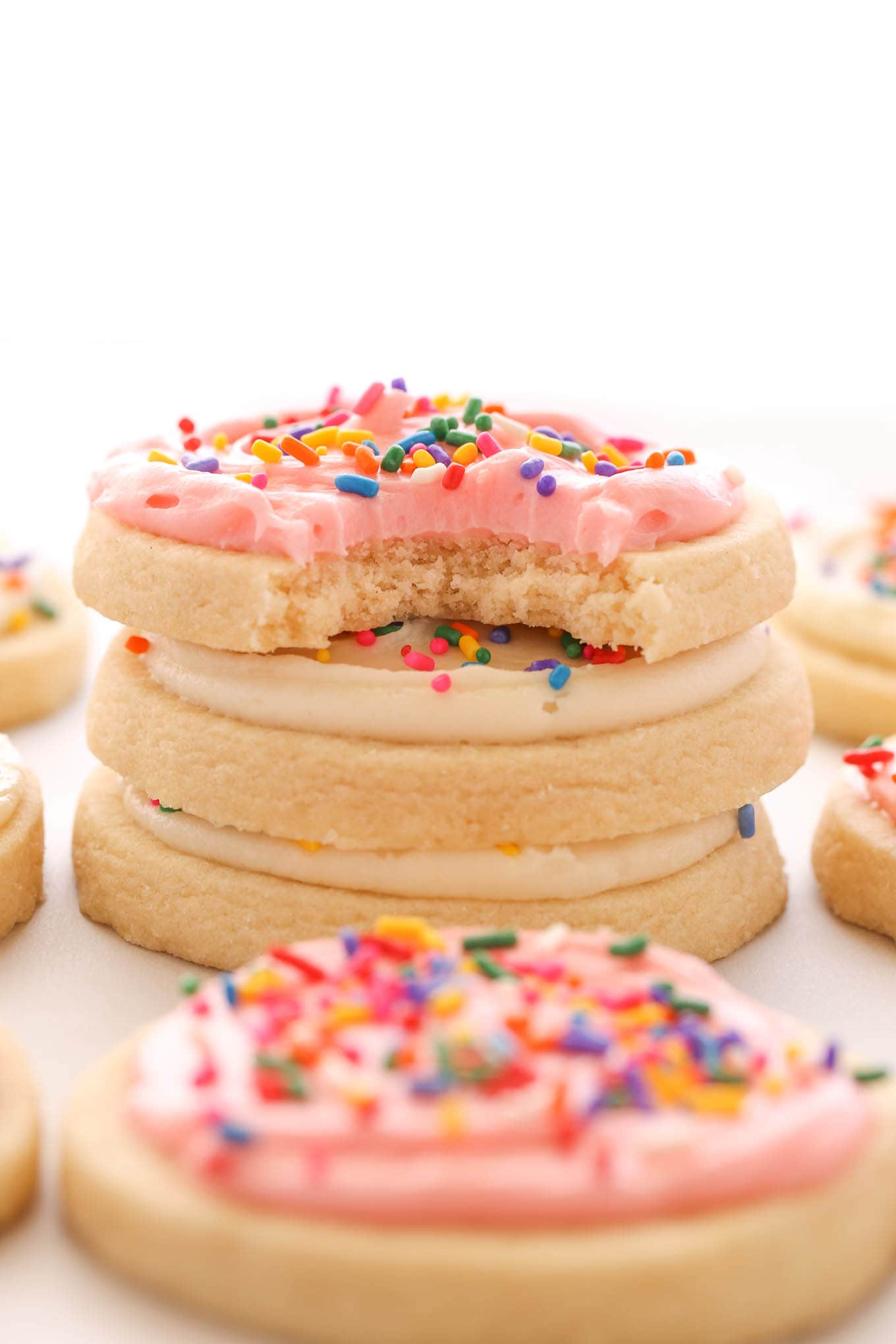 A stack of three soft cut out sugar cookies topped with frosting. Additional cookies surround the stack. 