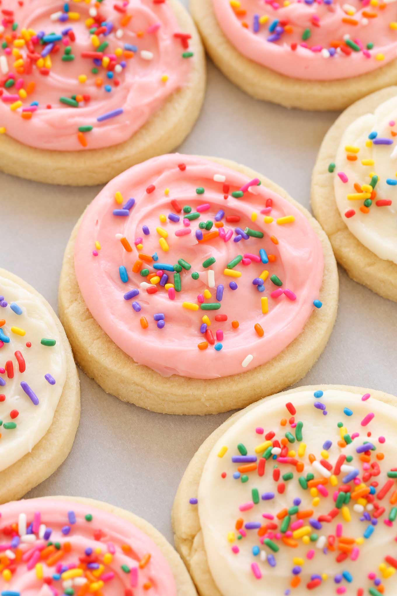 Overhead view of soft frosted sugar cookies topped with rainbow sprinkles. 