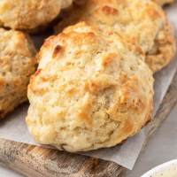 Several drop biscuits on top of a wooden cutting board topped with a piece of parchment paper.