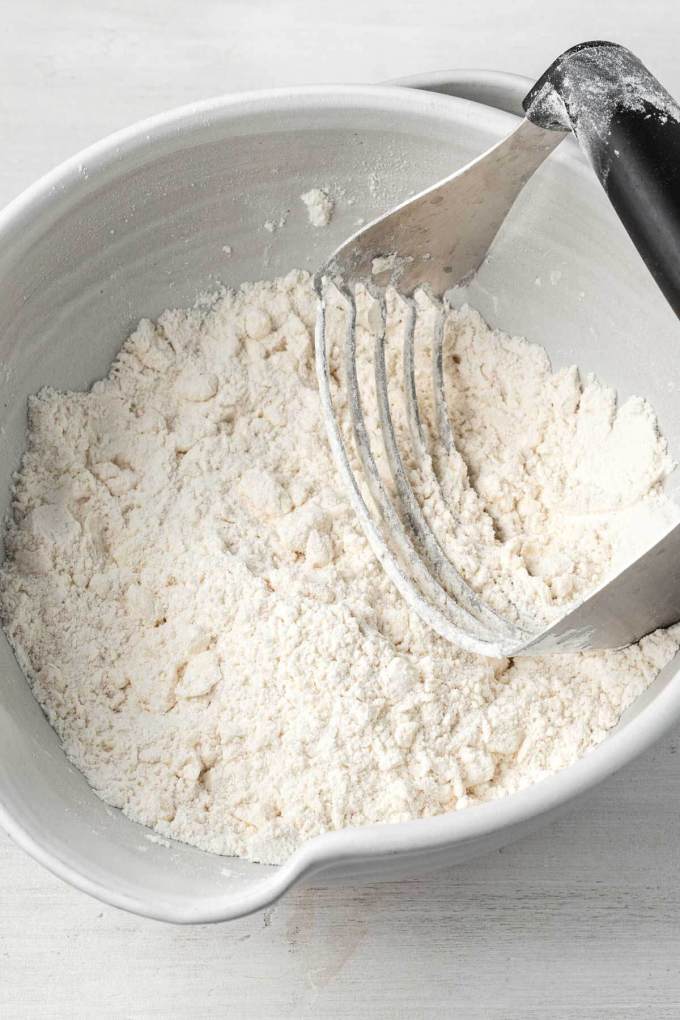 An overhead view of butter being cut into a flour mixture to make biscuits.