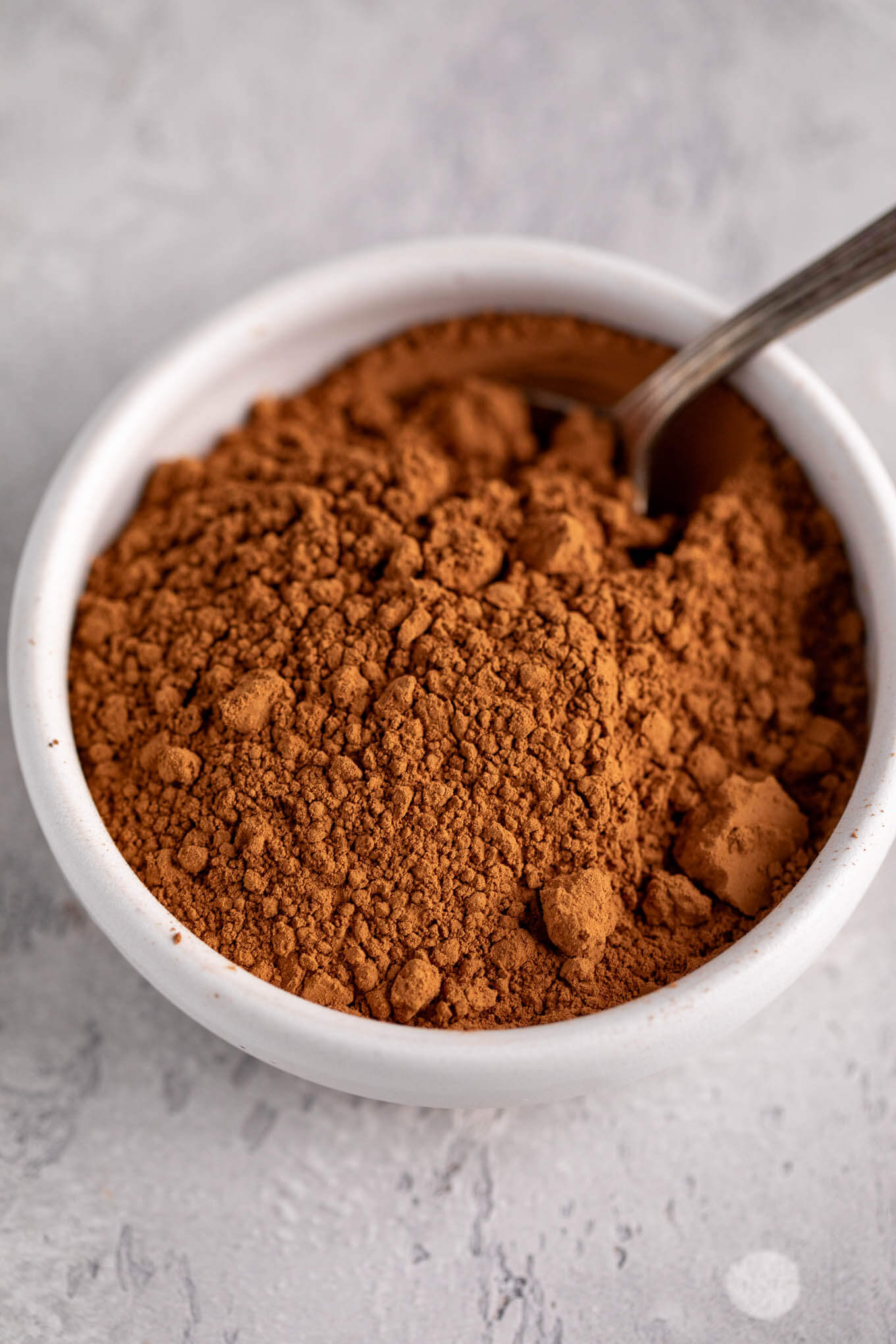 Natural cocoa powder inside of a white bowl with a spoon inside of it.