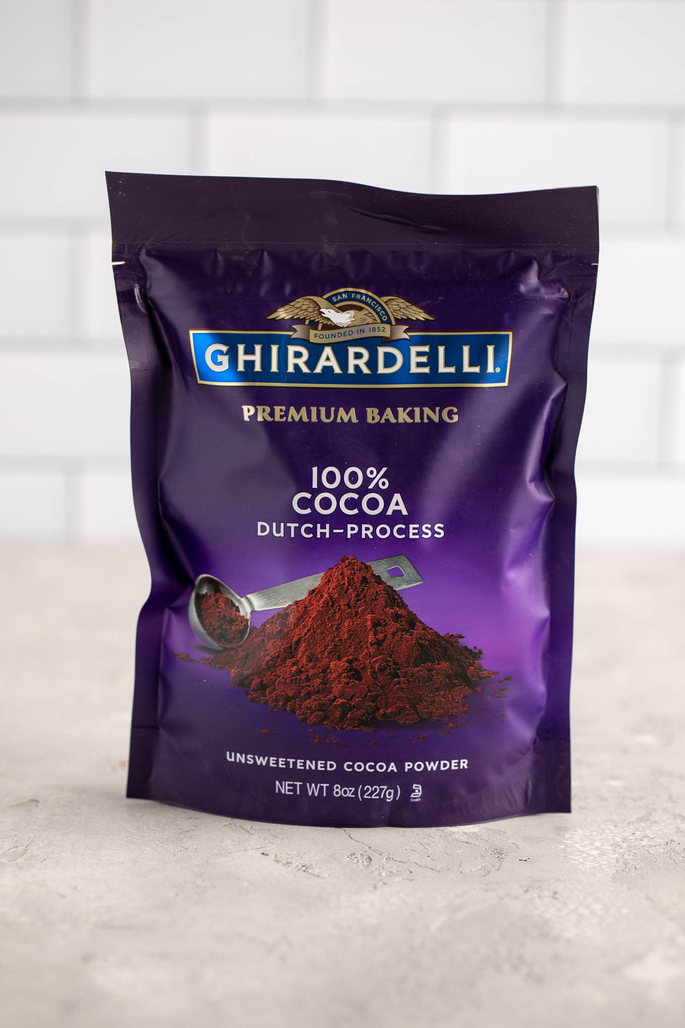 A package of Ghirardelli Dutch process cocoa powder on a gray surface.