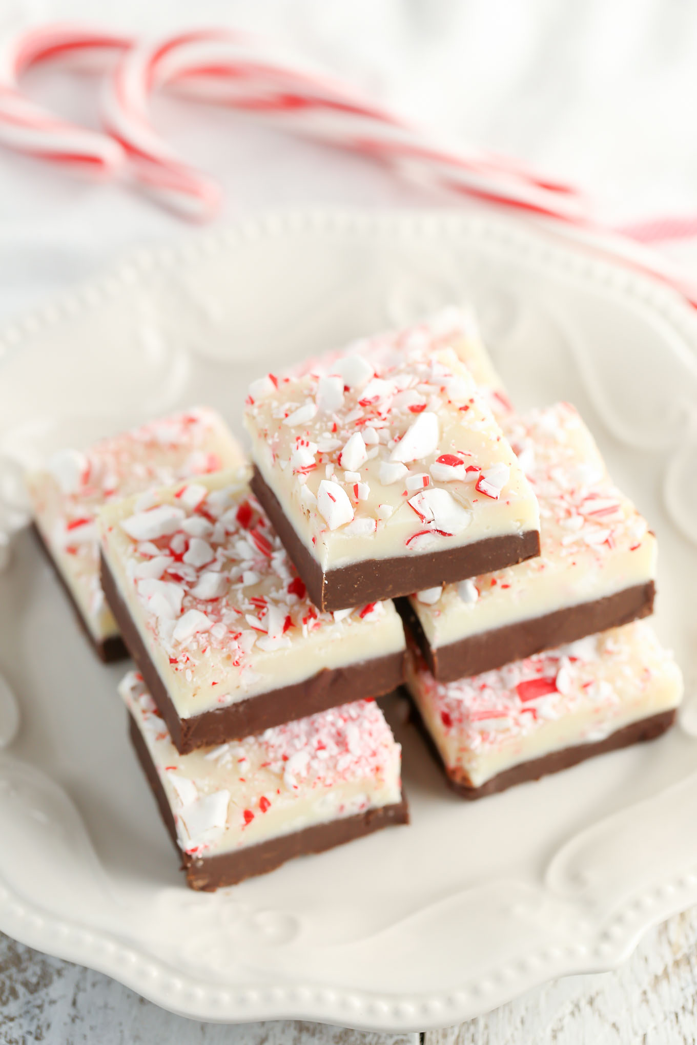 Stack of Christmas fudge on a white plate. Two candy canes rest in the background. 