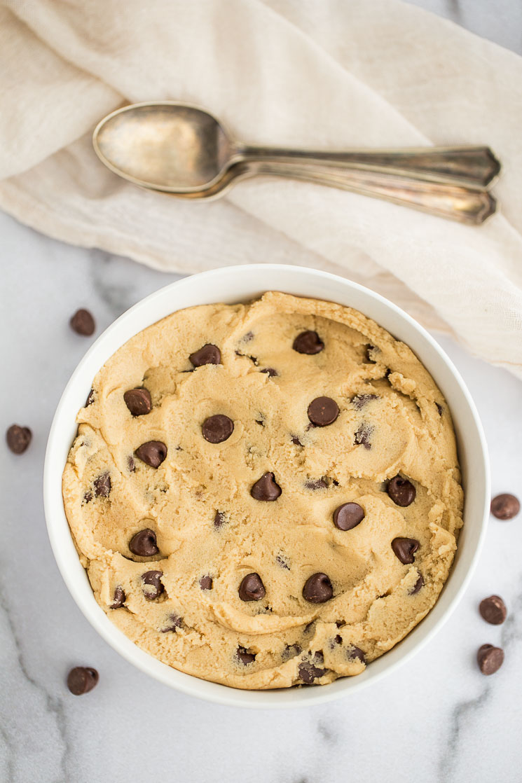 A white bowl filled with cookie dough and two spoons beside it.