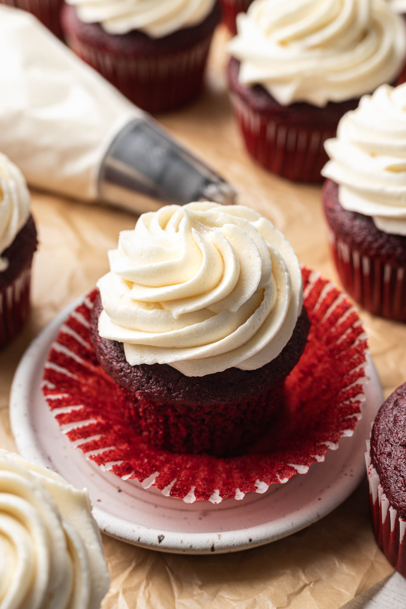 A close up look at a red velvet cupcake topped with ermine frosting, with the cupcake liner pulled down. 